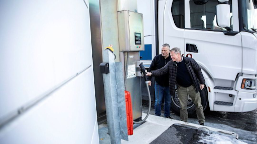 A picture containing 2 men standing and reaching out for gas